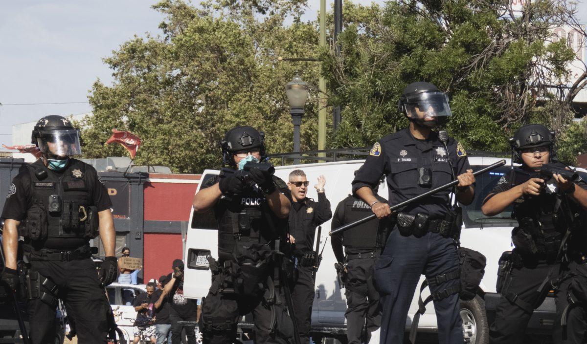 San Jose police officers in riot gear and geared up with batons and rubber bullet guns push protesters back during the May 29 George Floyd protest on Santa Clara Street. Christian Trujano/ Spartan Daily