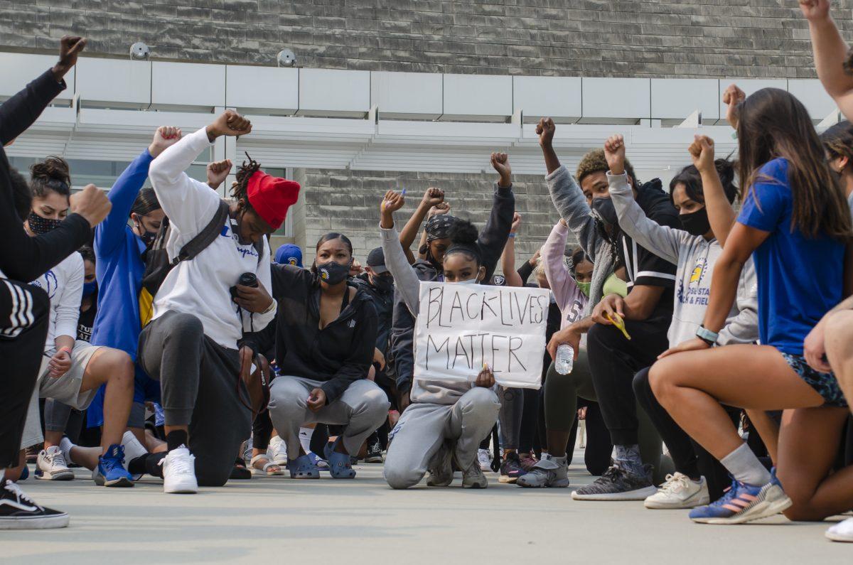 SJSU student-athletes kneel and raise their fists on Tuesday in a moment of silence during the peaceful march organized by the football team. Blue Nguyen | Spartan Daily 