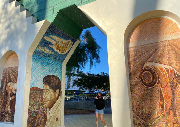 Una estudiante camina bajo el arco conmemorativo de Ces&#225;r Ch&#225;vez con una m&#225;scara de tela para protegerse de la exposici&#243;n al COVID-19 y el aire aire humeante.