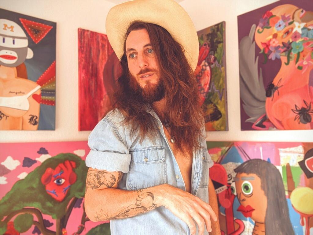 Creative writing master's student Matty Heimgartnerposes in front of his art at his studio in East San Jose.