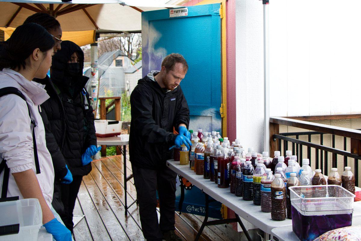 Campus Community Garden coordinator Matthew Spadoni names the natural tie-dyes inside of water bottles to students on Tuesday morning.