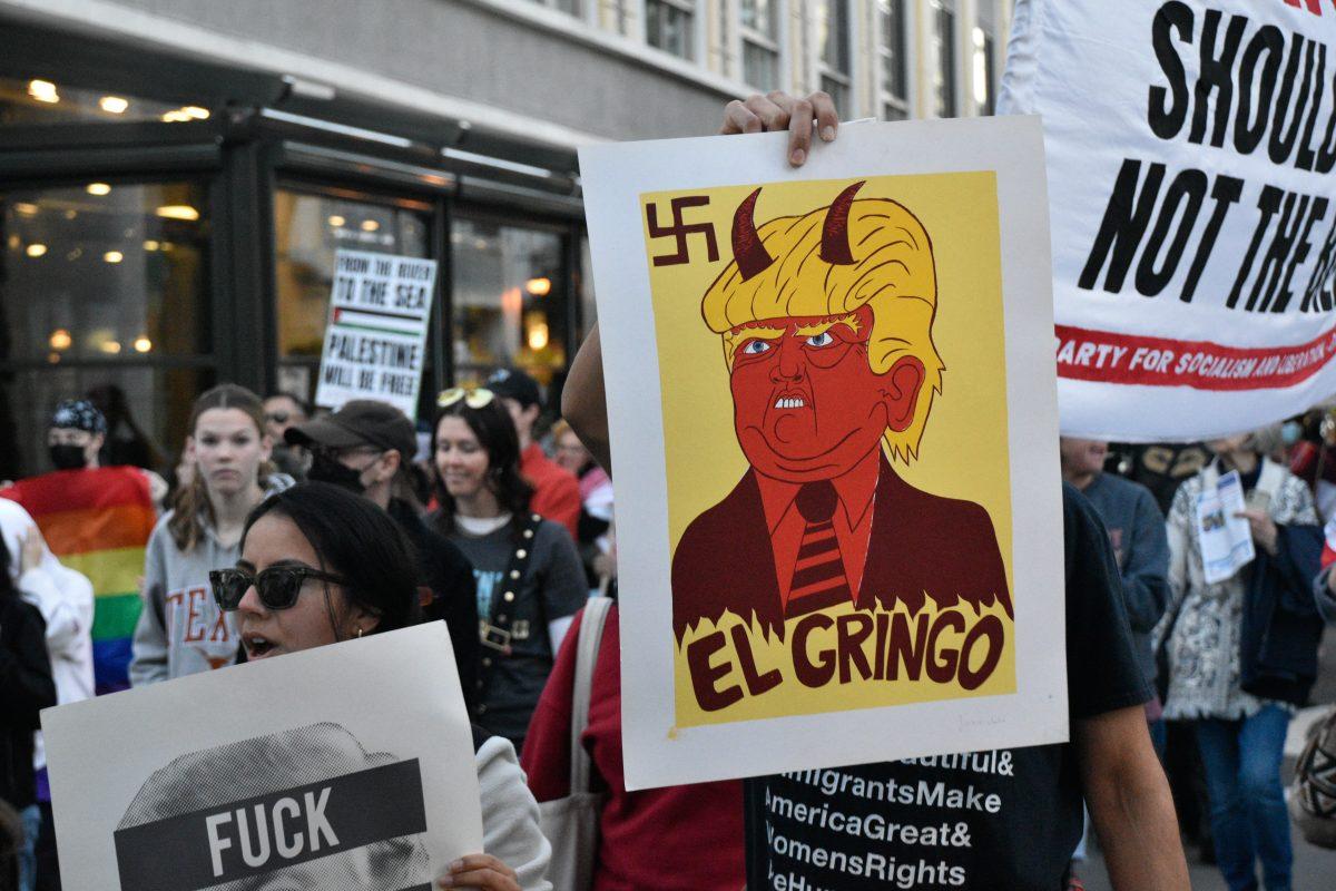 A protester holds up a cartoon of Trump with a sign that reads in Spanish, "El Gringo" while the crowd of protesters marches through Santana Row on Monday.