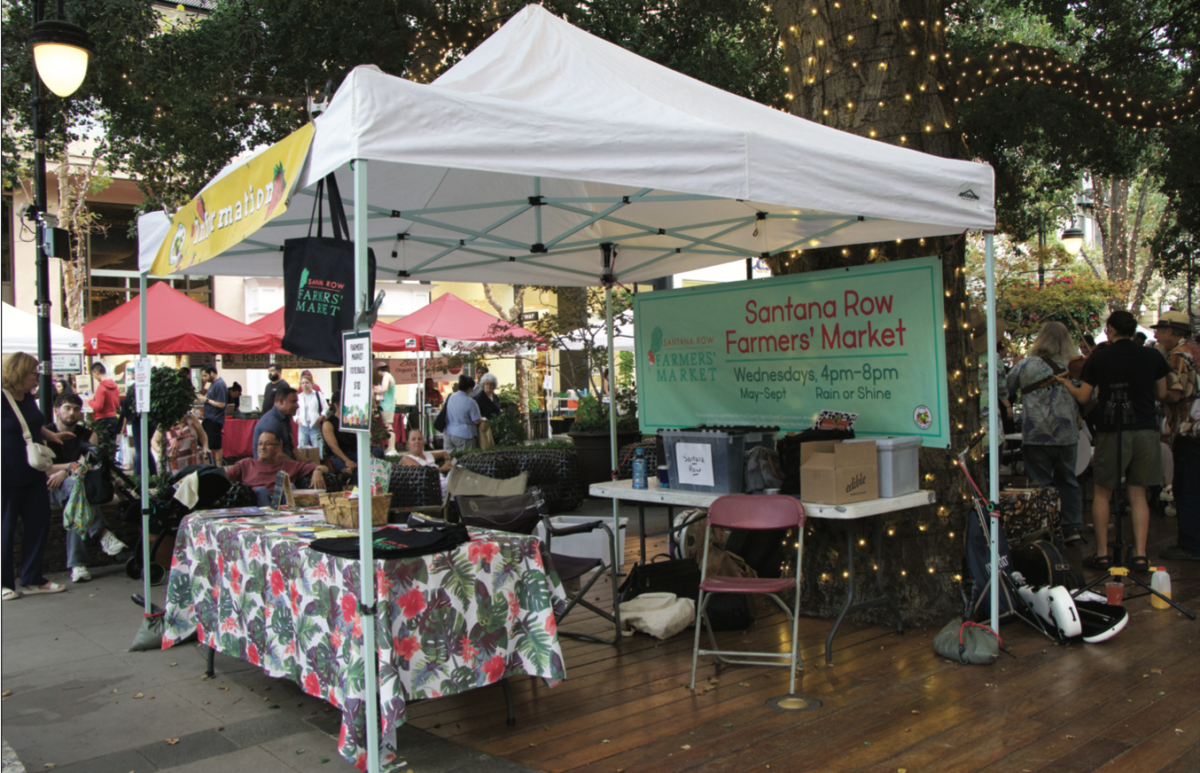 Community members relax and talk while surrounding the Santana Row Farmers’ Market information booth on Wednesday evening.