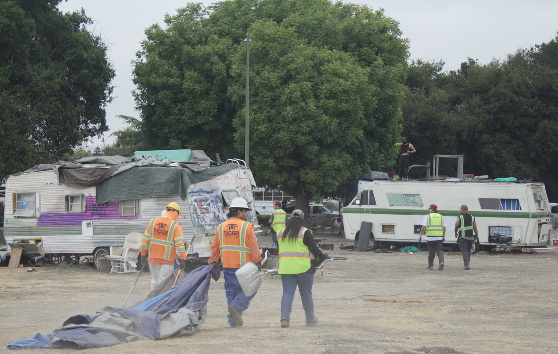 A San José resident stands atop an RV while being approached by city contractors who have been tasked with clearing Columbus Park.