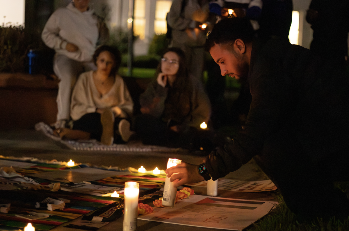 A student lights candles next to a placard reading, "No human is illegal on stolen land" at the vigil on Smith and Carlos lawn.