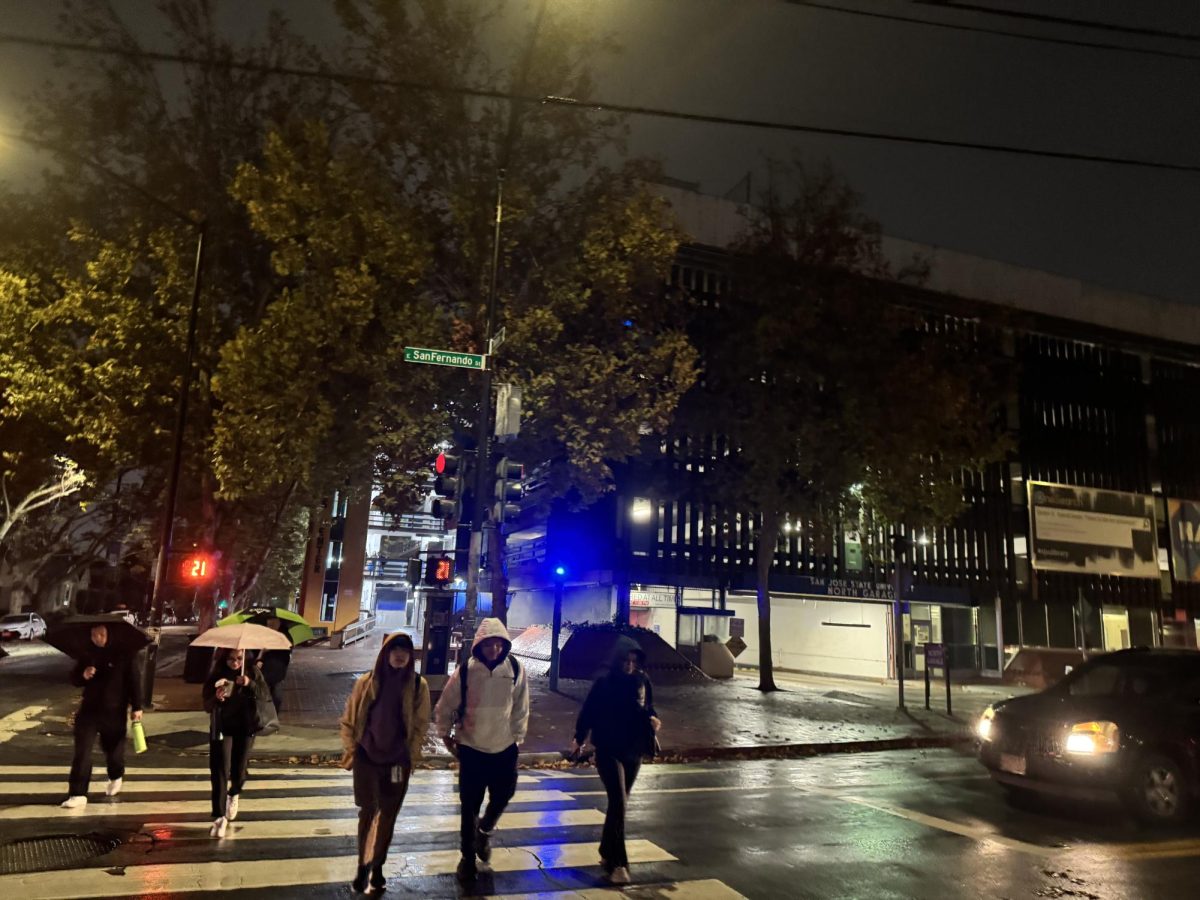 Students cross East San Fernando Street by the North Garage to get to the San José State University campus in the rain.