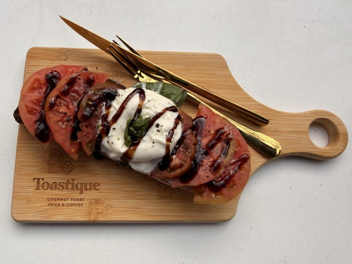 Toastique's gourmet Tomato Burrata toast plated on the business' custom engraved wooden cutting board. 