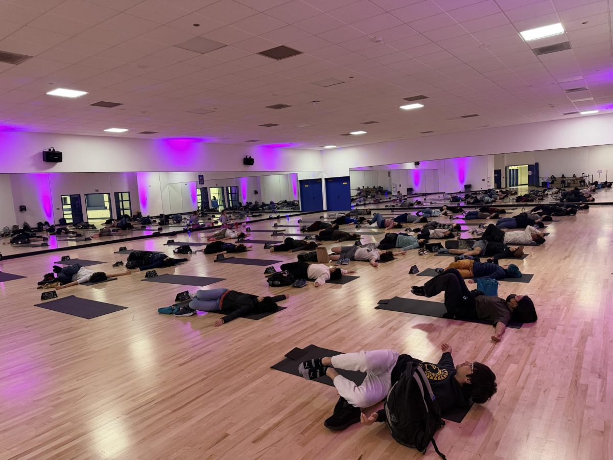 Students attempt a supine spinal twist exercise with help from yoga instructor Kate McCoy at Yoga and Boba.